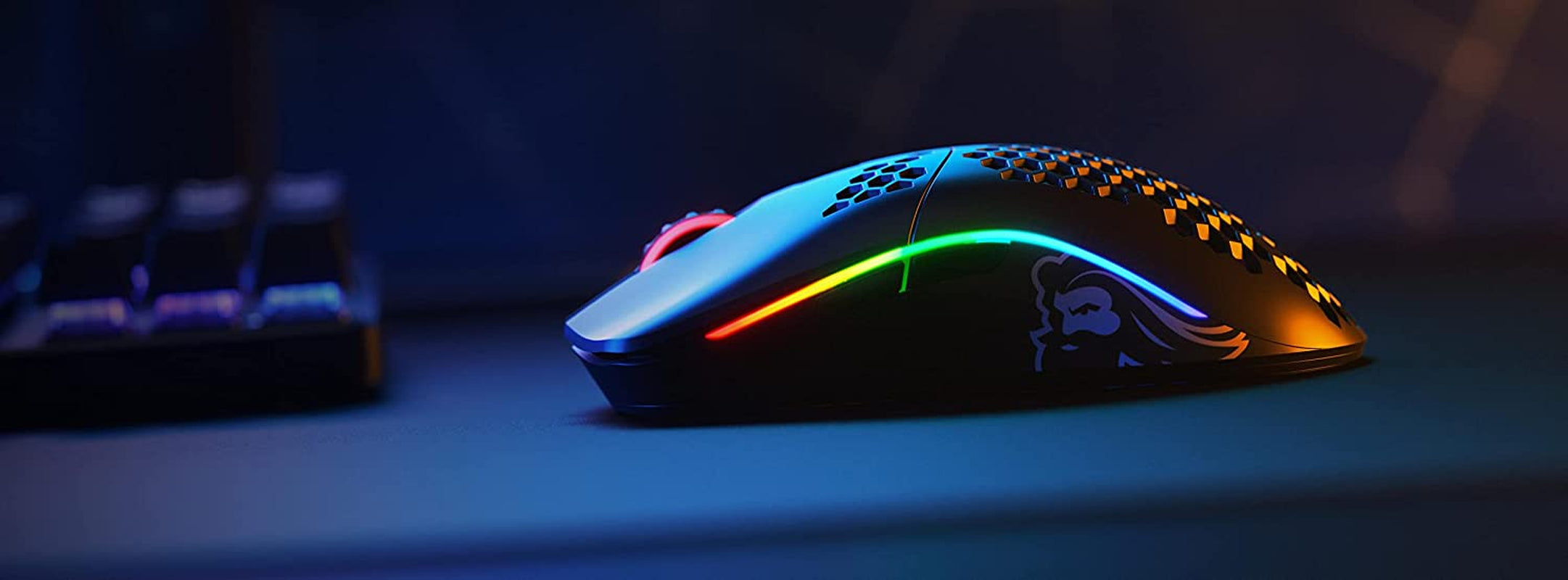 Glorious Model O Wireless Gaming Mouse on desk next to mechanical keyboard showcasing customizable RGB lighting