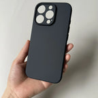 Hand holding BESDYNASTY matte black silicone iPhone 16 Pro Max case showing back view straight on, large square triple camera cutout with three circular lens openings and LiDAR scanner hole clearly visible, smooth matte TPU finish, against light gray background