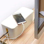 Cable management box on wooden table organizing USB-C cable that is charging a smartphone