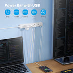 TROND power strip wall-mounted above a dual monitor developer desk setup with laptop and smartphone charging, with spec icons showing 4 AC outlets, 3 USB-A ports, 1 USB-C port, 6ft cord, and 1440J surge protection