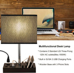 Briever desk lamp with linen shade, wooden base with 3 phone slots, USB charging ports, and AC outlets, next to a laptop on a wooden desk
