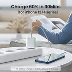 White 30W USB-C wall charger plugged into a white multi-outlet power strip on a round white coffee table, connected via white USB-C cable to a blue iPhone 12 lying flat on the table, with person in light blue sweater reclining on white sofa holding a tablet in background, bold text reading Charge 60% in 30Mins for iPhone 13 14 series, and fine print reading Ps: 30Mins charge to 50% for iPhone 8 to 14 series