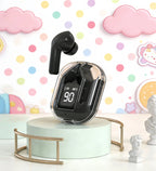 Black wireless Bluetooth 5.3 earbud in transparent charging case propped on a mint green cylindrical podium with gold wire stand, one black earbud ejected upright, LED display reading 90, with colorful polka dot wallpaper and pastel cloud and cartoon character decorations in background