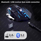 Black gaming mouse with blue RGB lighting on a dark grey textured surface, with a USB nano receiver and charging cable laid out below it, cyan text reading "Bluetooth + USB receiver dual-mode connection" at the top, and a white pill badge at the bottom showing a USB icon labeled "2.4G Wireless" and a Bluetooth icon labeled "5.2 Bluetooth"