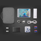 OrgaWise Grey Portable Three-Layer Electronics Organizer next to tablet, power bank, cables and other power accessories on a grey floor top-view