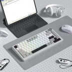 Minimalist desk setup featuring a compact mechanical keyboard with creamy white and gray shine through PBT keycaps, alongside a mouse, headphones, and laptop