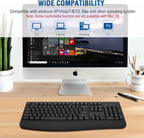 Black ergonomic wireless keyboard placed on a wooden desk in front of an iMac displaying a Windows 10 Start screen, with a potted plant and pencil cup in the background, bold blue text reading "Wide Compatibility" at the top, a subtitle reading "Compatible with Windows XP/Vista/7/8/10, Mac and other operating systems", a red note reading "Some multimedia functions are not available with Mac OS", and four blue icon badges labeled PC, Laptop, Desktop, and TV