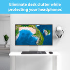 White over-ear headphones hanging on a TotalMount white wall mount hanger to the right of a large ultrawide monitor displaying an aerial island photograph, above a white standing desk with dark keyboard and mouse, with light blue banner reading Eliminate Desk Clutter While Protecting Your Headphones