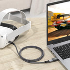 Laptop with a racing game on screen, connected to a white VR headset via USB-A to USB-C adapter on a wooden surface