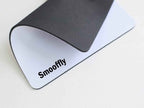 Smooffly galaxy gaming mouse pad folded back on a white surface to reveal the plain white non-slip rubber base with the bold black Smooffly logo printed in the bottom left corner, and the dark grey textured fabric surface visible curling over the top