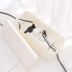 Cable management box with lid off concealing power strip and organizing cables on a white floor, top side view