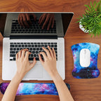 Person using a laptop with galaxy-themed wrist rest and mouse pad set on a wooden desk